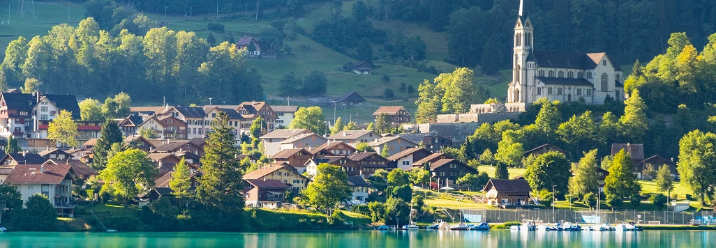 スイスの夏の山岳風景。青空と緑の草原、遠くに雪をかぶったアルプスの山々が見える。