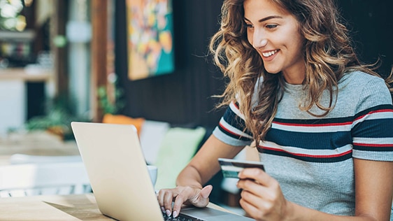 a woman holding a card facing a laptop