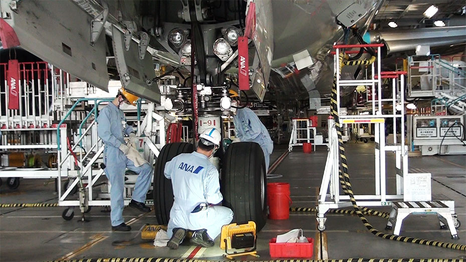 飛行機の前脚付近で作業する整備士たちの写真