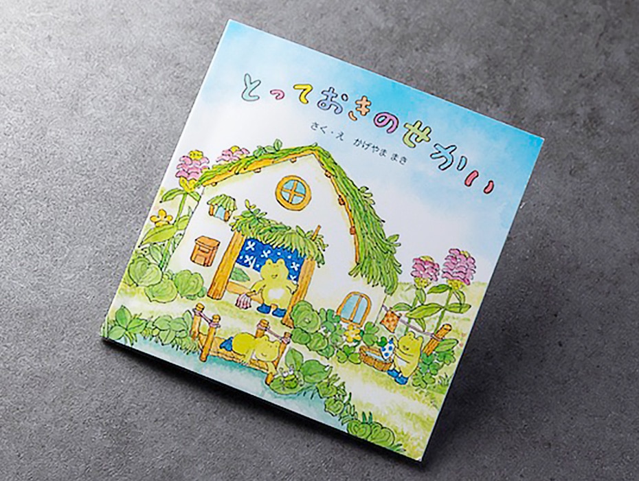 ANA Future Promiseをテーマにした絵本「とっておきのせかい」の表紙。3匹のかえるが池のほとりの小屋で洗濯をしたり掃除をしたりしている水彩画。