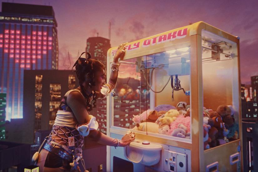 Woman playing a giant, building-sized "FLY OTAKU" claw machine standing among neon skyscrapers.